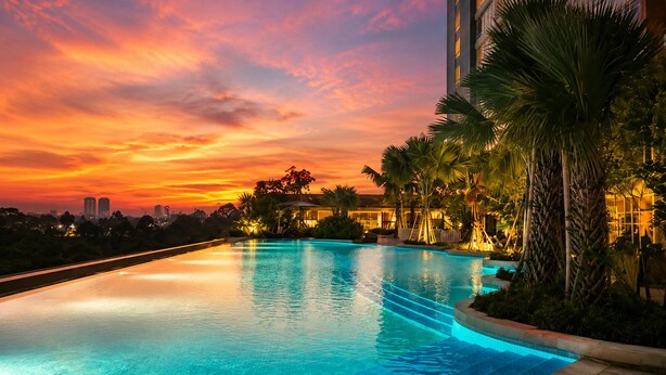 A swimming pool at sunset with a view of a city skyline and palm trees.