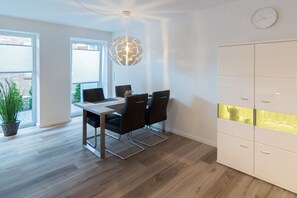 Uma área de refeições moderna com uma mesa de vidro, cadeiras pretas e um lustre globo.