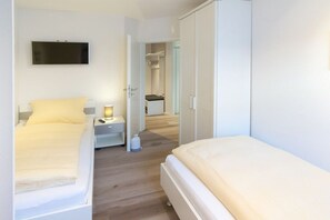 Quarto com duas camas, televisão, mesa de cabeceira com abajur e guarda-roupa.