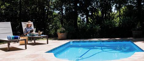 Una piscina con borde de baldosas, rodeada de exuberante vegetación y árboles.