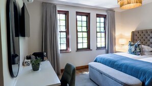 A hotel room with a bed, a desk, a chair, a TV, and a window with curtains. - Vendome Wine Estate (Paarl)