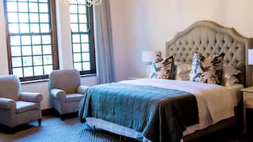 Ett hotellrum med en stor säng, två fåtöljer, en kristallkrona och utsikt över omgivningarna genom stora fönster.