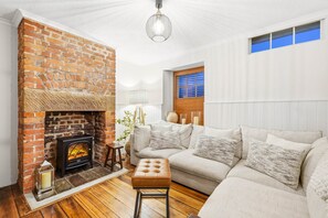 Una sala de estar con chimenea de ladrillo, un sofá, piso de madera y una lámpara colgante.