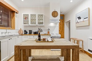 Una cocina moderna con armarios blancos, una mesa de comedor de madera y un amplio ventanal con persianas.