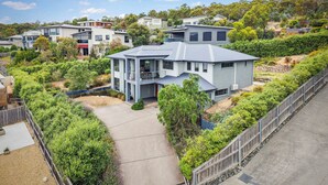 A modern two-story house with a balcony, surrounded by lush greenery and a paved driveway. - 4 Bedroom House - Gorgeous View (Tranmere)