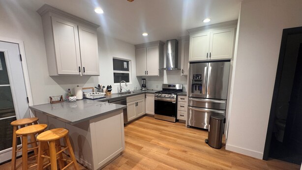 A modern kitchen with white cabinets, stainless steel appliances, a central island with stools, and wooden flooring. - Charming 2-bedroom house with WiFi, AC in welcoming Long Beach (Long Beach)