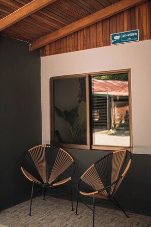 A room with two black and wooden chairs, a large window with a view of a red-roofed building, and a wooden ceiling. - Dominical Long Term Rental (Bahía Ballena)
