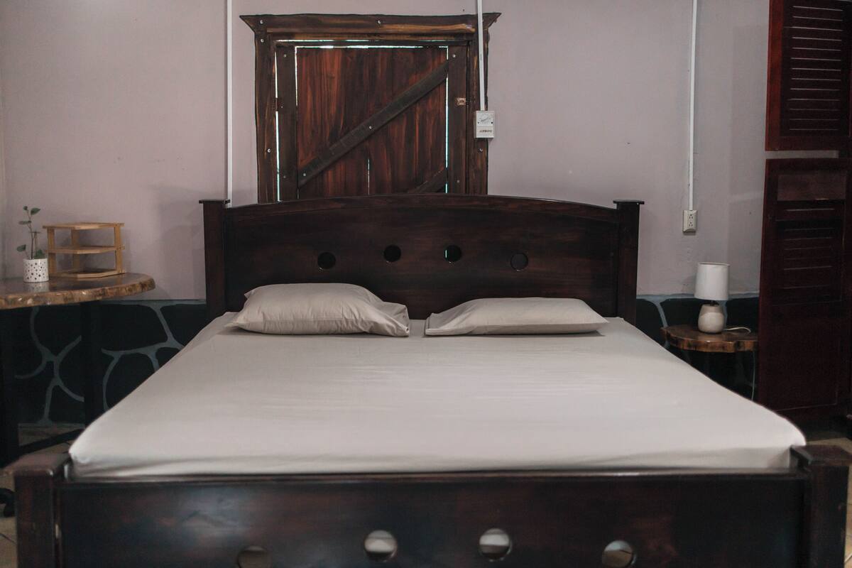 Una cama con cabecera de madera, dos almohadas y una colcha blanca.