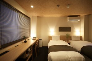 A hotel room with two beds, a desk with chairs, a window with blinds, and an air conditioning unit. - Hotel akari (Kyoto)