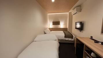 Habitación de hotel con dos camas individuales, un escritorio con silla, televisión e iluminación en el techo.