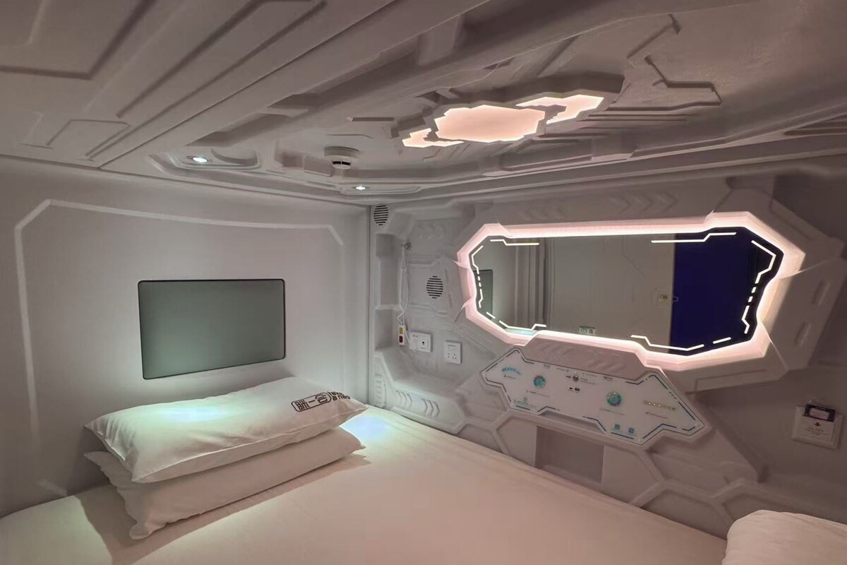 Una habitación con cama, televisor montado en la pared y un espejo hexagonal único con iluminación integrada.