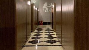 Ein Hotelgang mit Holzwandverkleidung, einem Schachbrettmuster-Boden und einer Wandleuchte.