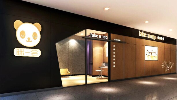 Eine moderne Hotelhalle mit einer 'Take a Nap'-Lounge, ausgestattet mit einer Couch und einem kleinen Tisch.