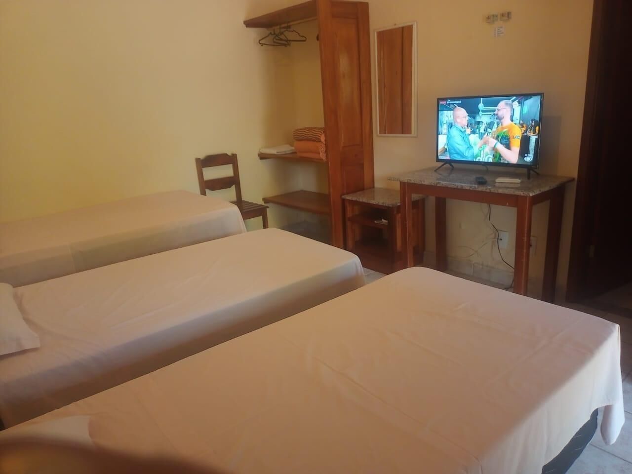 Una habitación con dos camas individuales, un escritorio de madera, un televisor y una silla.