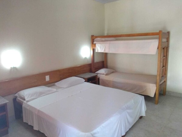 A room with two single beds and a bunk bed, all with white bedding. There are two bedside tables and a wall-mounted light fixture. - Patipe Praia Hotel (Canavieiras)