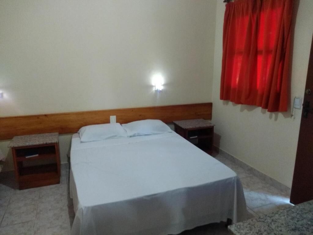 A simple bedroom with a bed, wooden headboard, bedside tables, and a red curtain.