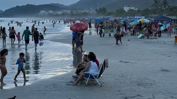 Una playa concurrida, gente caminando y sentada bajo sombrillas.