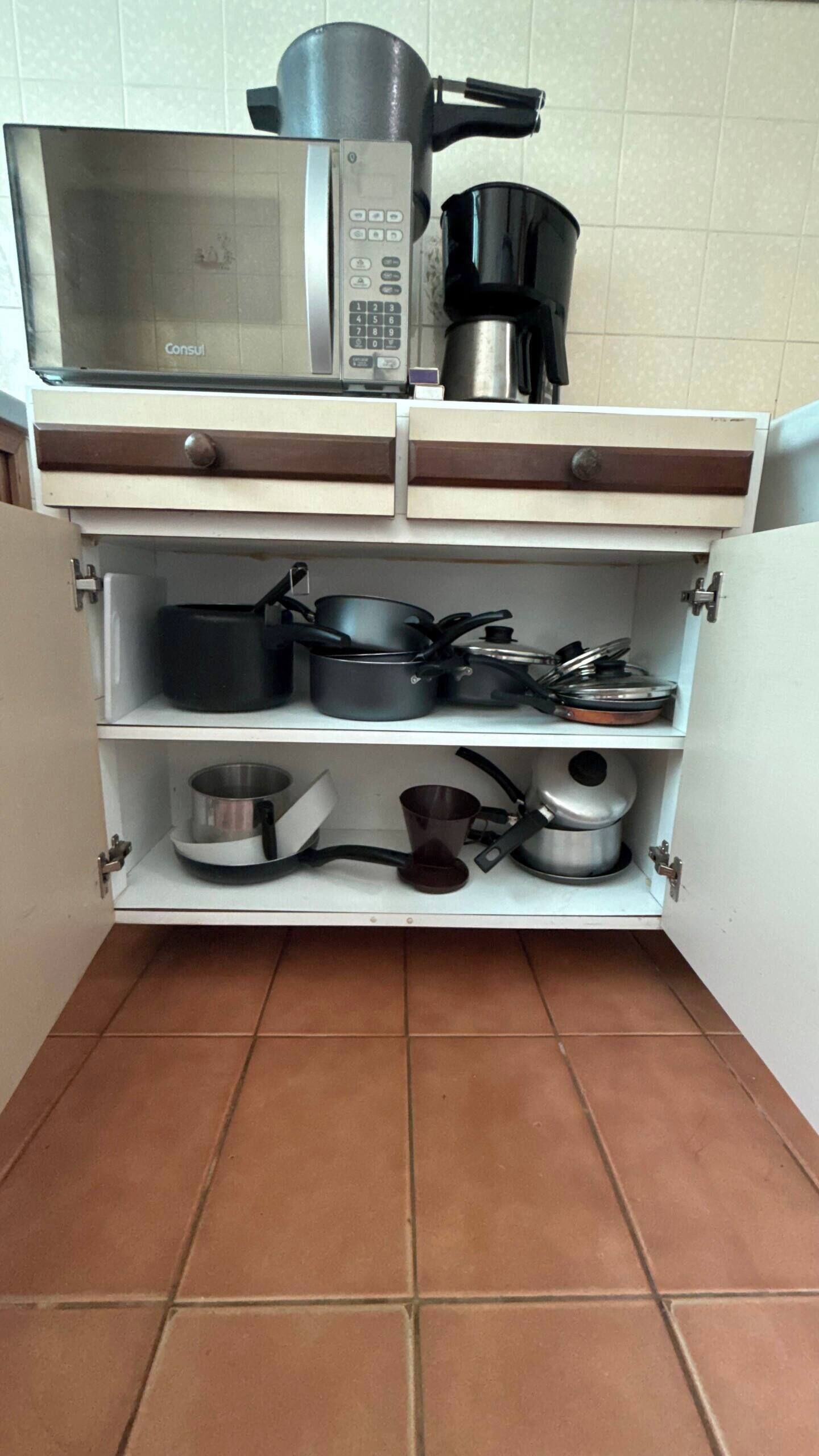 A kitchen with a microwave, coffee maker, and various pots and pans on shelves.