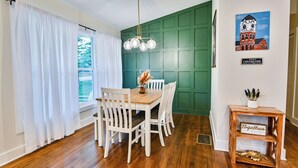 Un coin repas avec une table en bois et des chaises blanches, un mur d’accent vert et une pancarte indiquant « Bienvenue à Covington ».