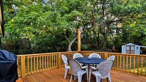 Une terrasse en bois avec une table et des chaises, entourée d’arbres et d’une clôture.