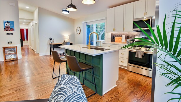 Une cuisine moderne avec un îlot central, un plancher en bois et une grande fenêtre.