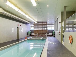 Ein moderner, überdachter Pool mit gut sichtbarer Beschilderung, einer Holzabtrennung und Sicherheitsausrüstung.