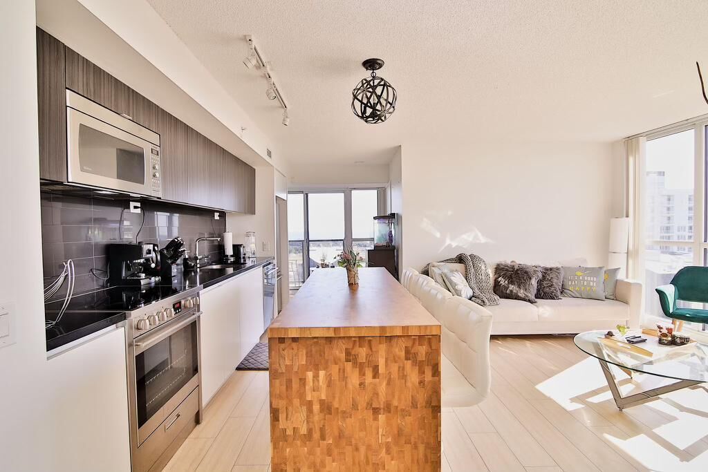 Una cocina moderna con una isla central, una zona de comedor con mesa de vidrio y una sala de estar con sofá y sillón verde.