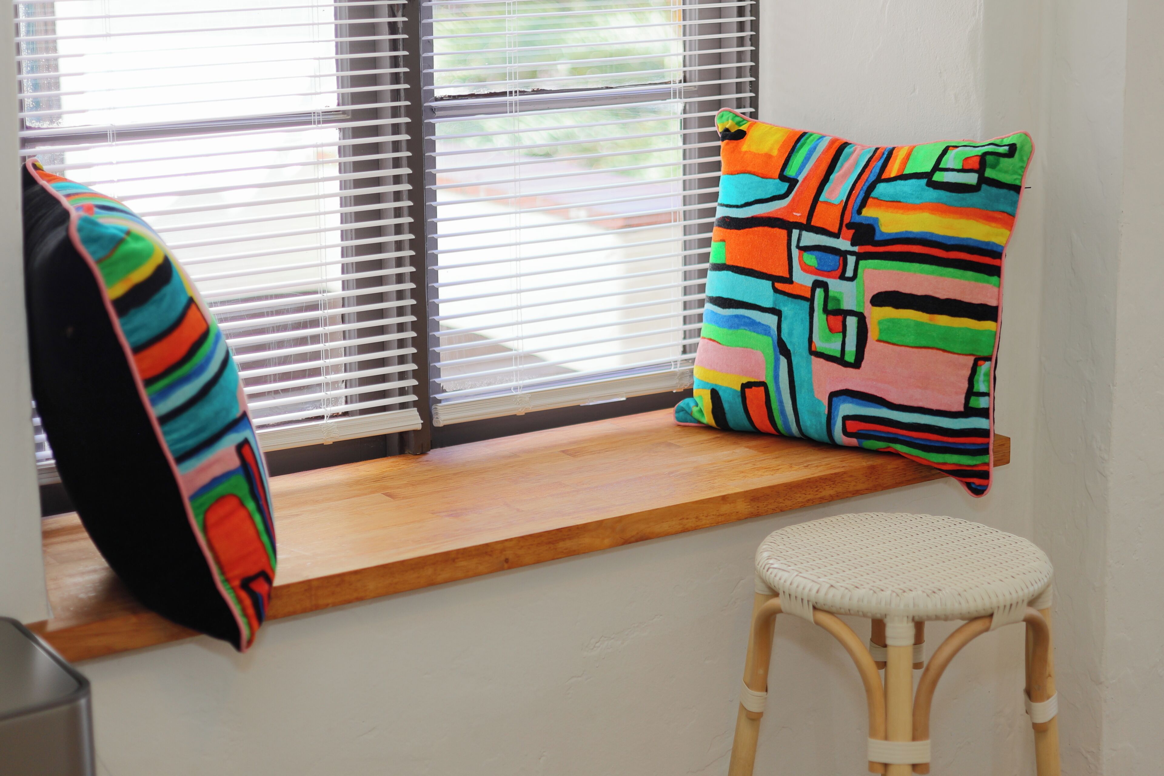 A room with a window seat, colorful striped pillows, and a wicker chair.