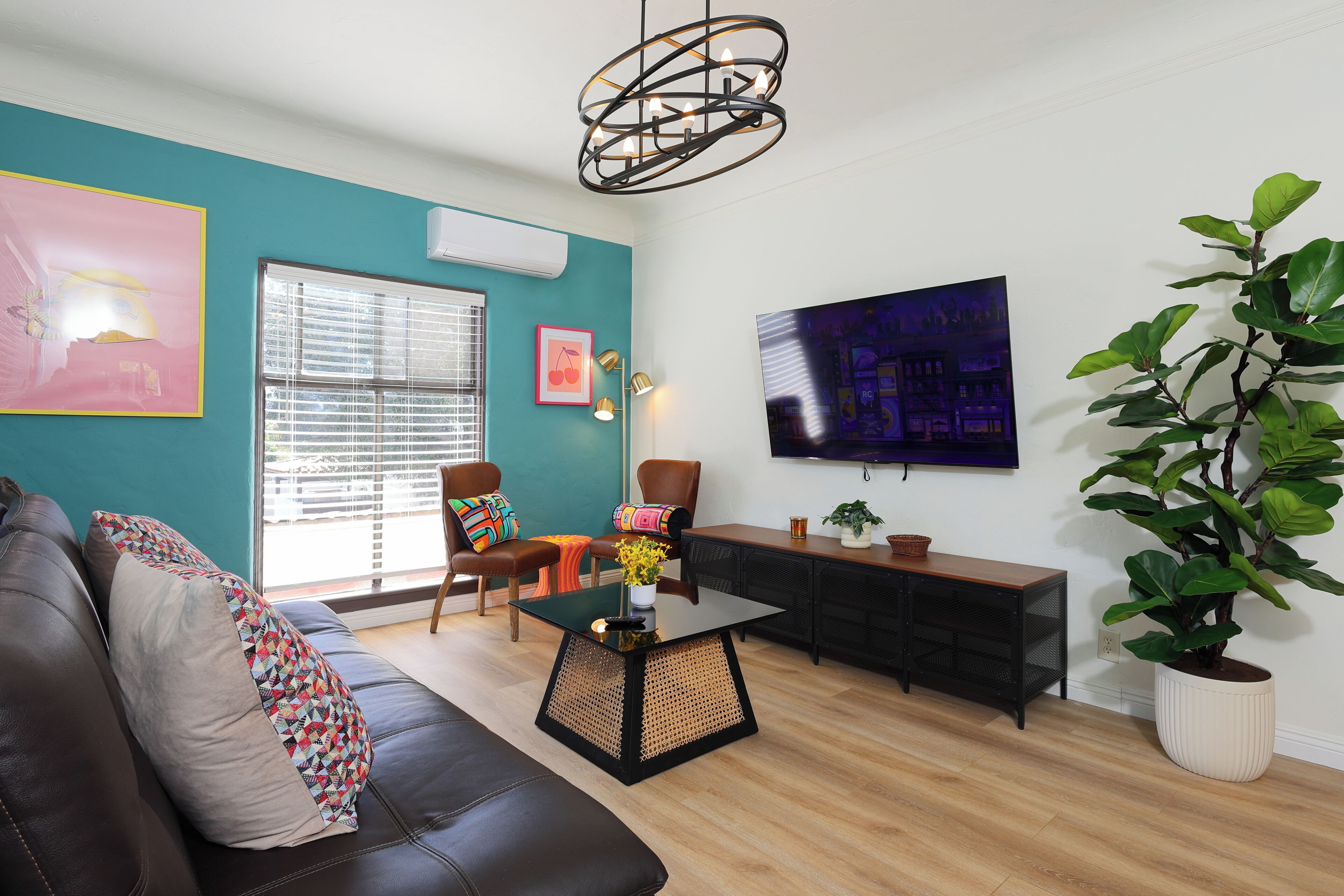 A living room with teal walls, a black leather sofa, a glass coffee table, a wooden side table, and a large potted plant.