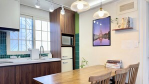 Moderni keittiö, jossa on puukehikot, valkoinen jääkaappi, mikroaaltouuni ja ruokapöytä tuoleineen. Ikkunasta on näkymä ulos, ja seinällä on kuva Eiffel-tornista.
