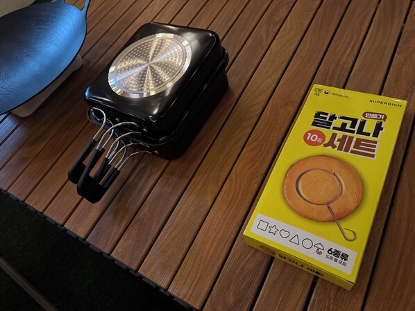 A black portable heater with a circular vent on a wooden table. Next to it is a yellow box with Korean text and an image of a round object with a hook. - Rooftop Relaxation with Music, Movies & Vibes, 6 minutes from Itaewon St, (Seoul)