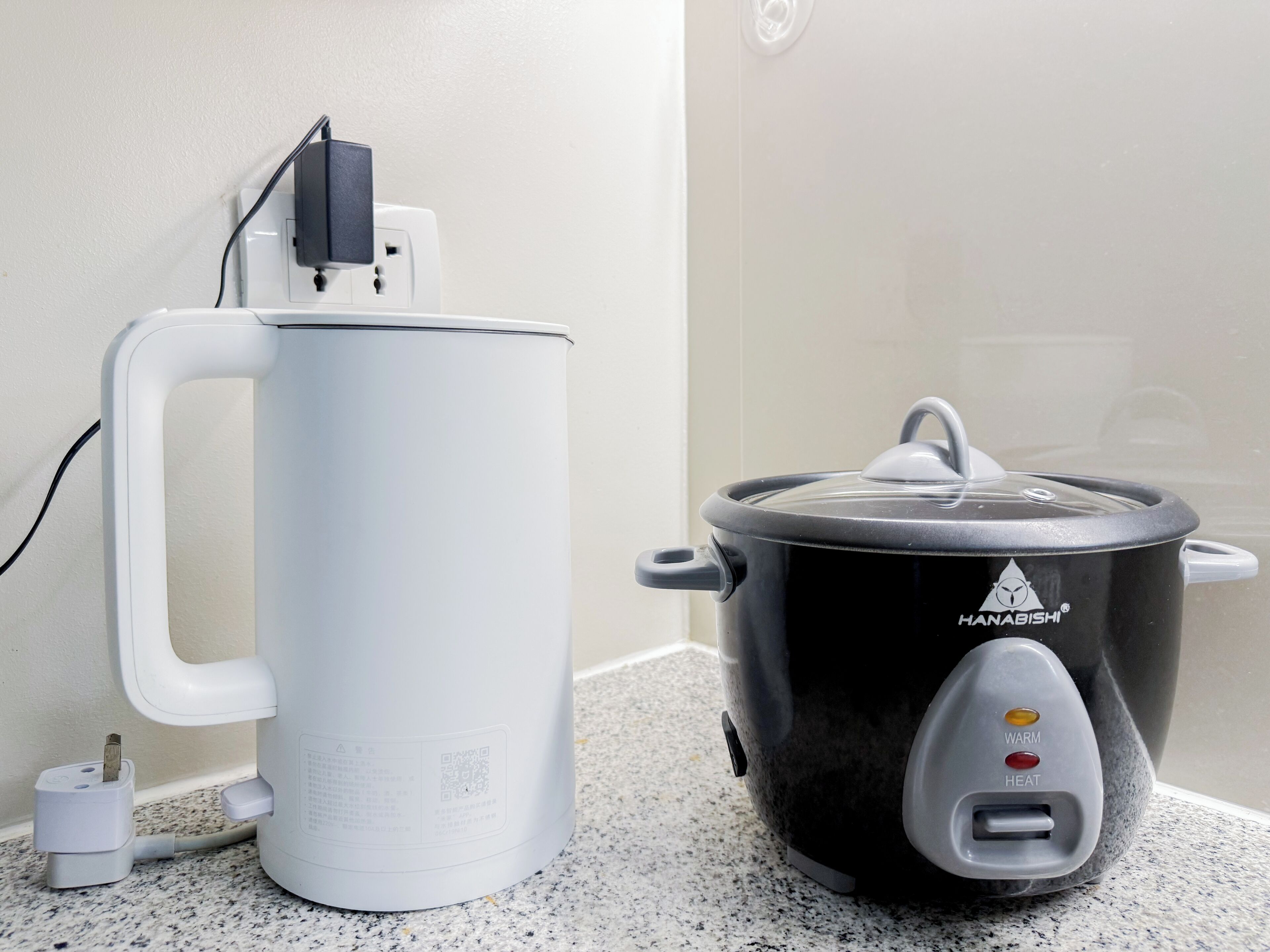 Una tetera eléctrica blanca y una olla de cocción lenta negra sobre una encimera de cocina.