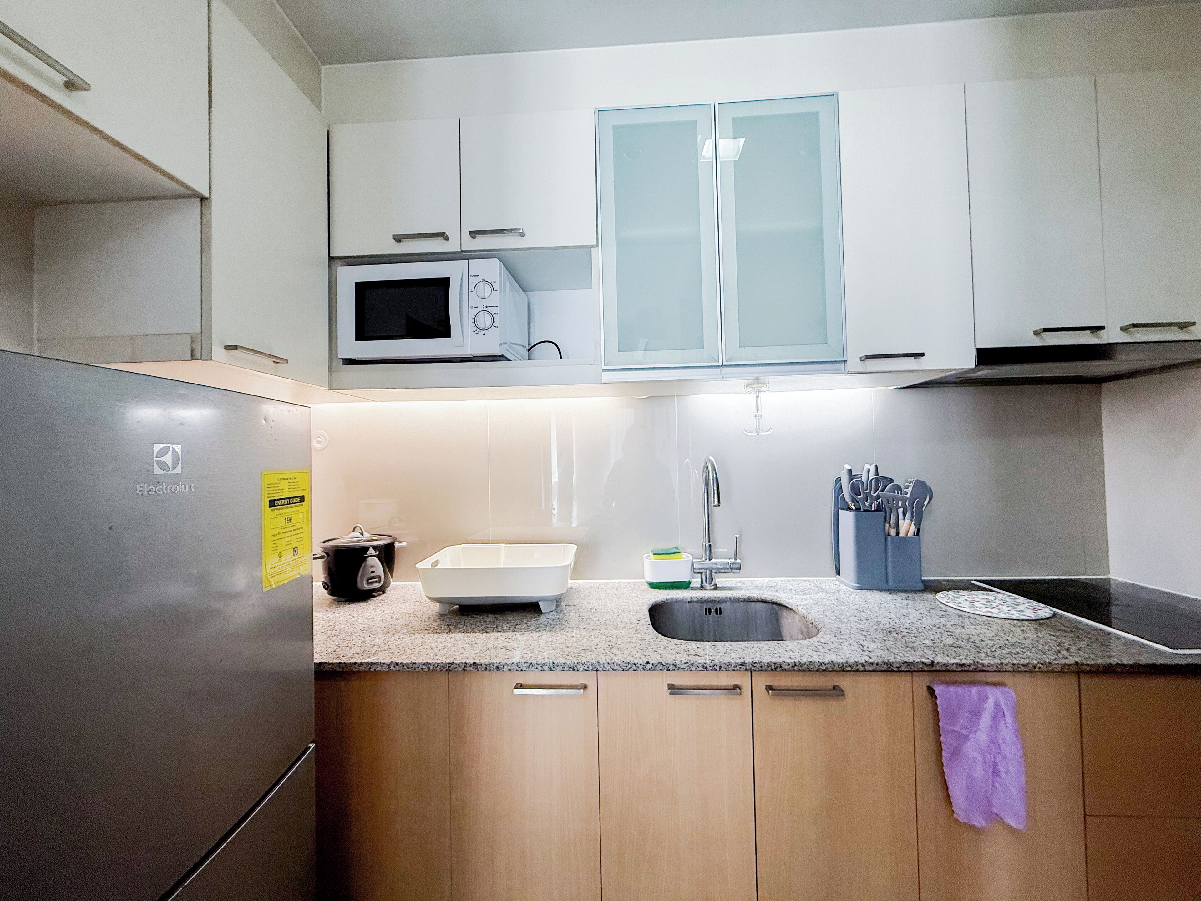 A kitchen with a stainless steel refrigerator, a microwave, a sink, and wooden cabinets.