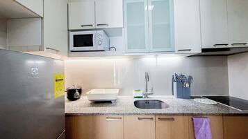 A kitchen with a stainless steel refrigerator, a microwave, a sink, and wooden cabinets.
