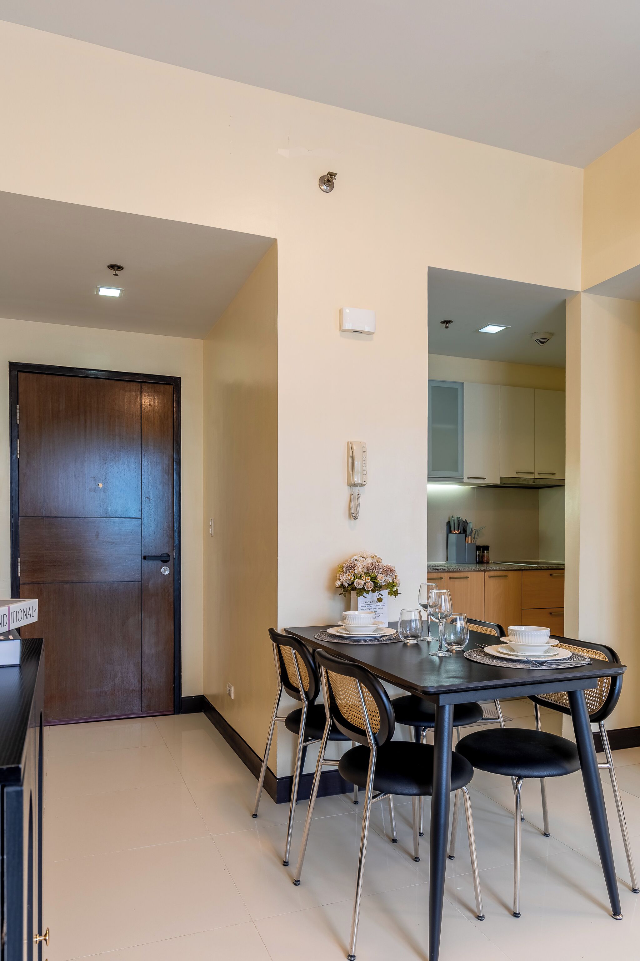 A dining area with a table set for four, a kitchen in the background, and a door to the left.
