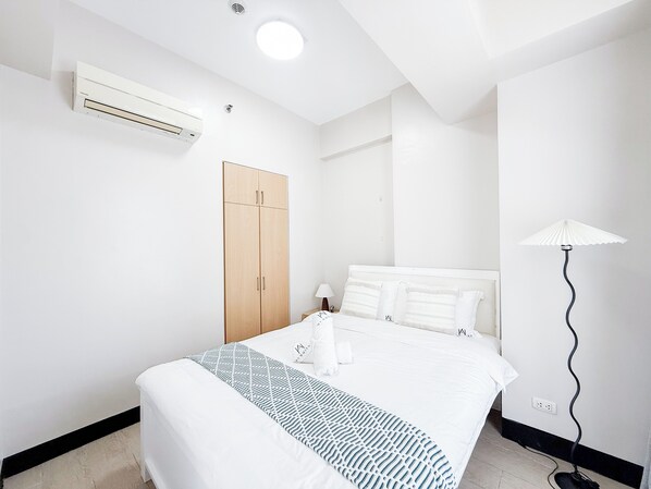Quarto de hotel com cama, guarda-roupa, ar condicionado, luminária e tomada.