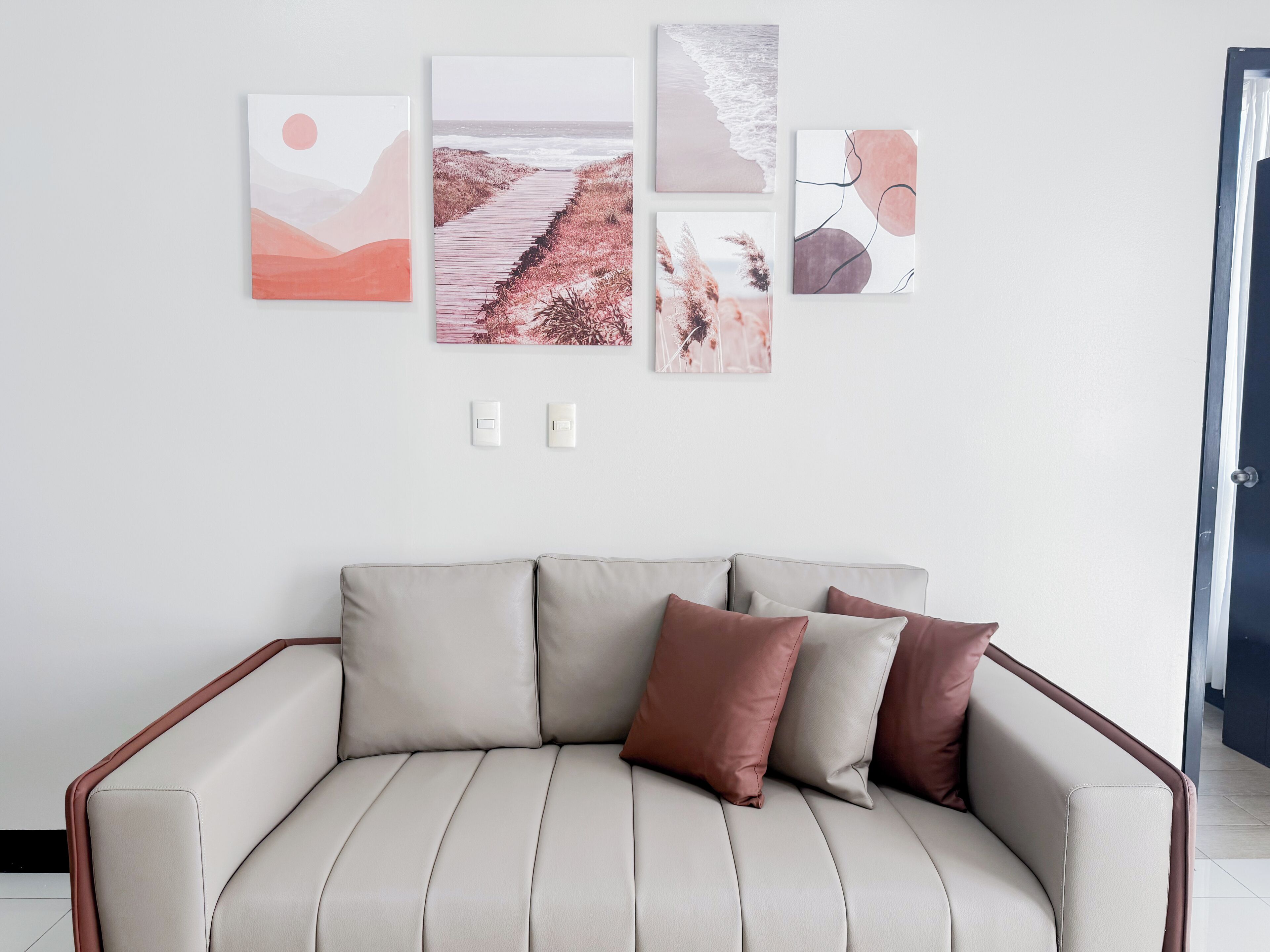 Ett modernt vardagsrum med en beige soffa, en tavla som föreställer en stig genom en skog och en tavla med ett strandmotiv.