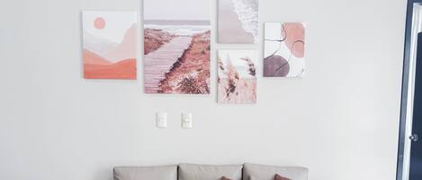 Ett modernt vardagsrum med en beige soffa, en tavla som föreställer en stig genom en skog och en tavla med ett strandmotiv.