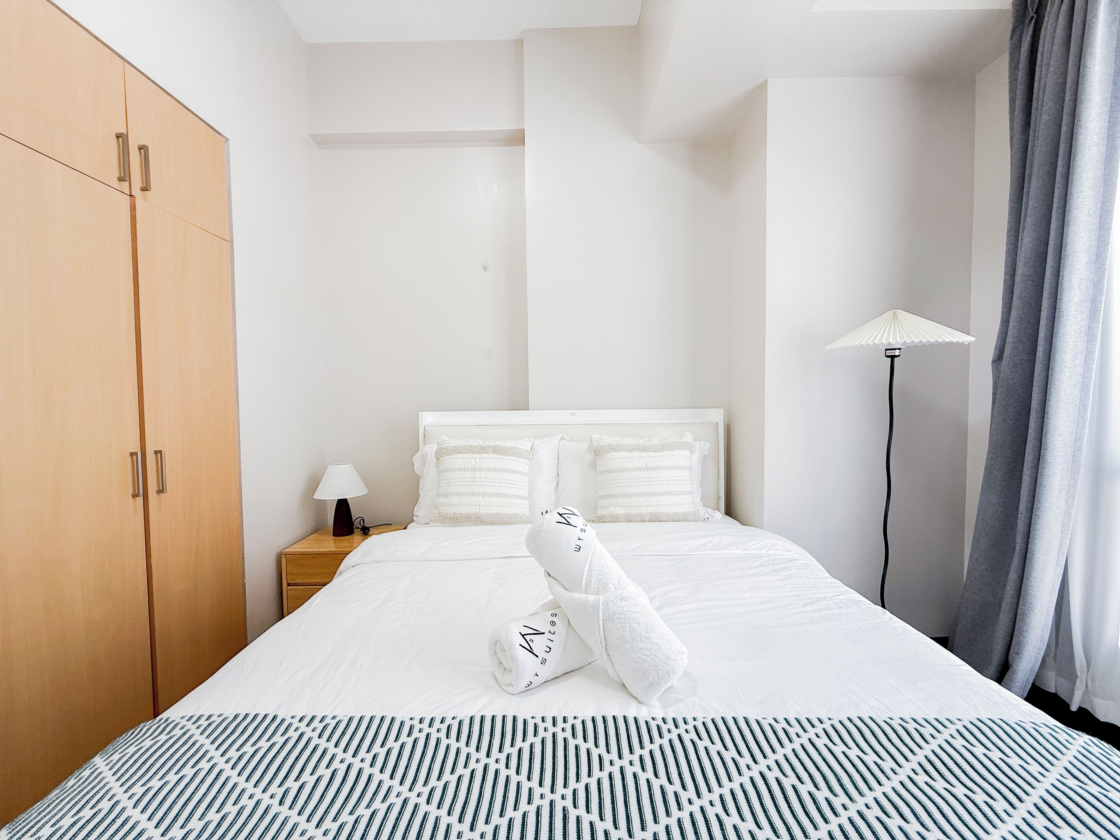 Une chambre d’hôtel comprenant un lit, une table de chevet, une lampe, une armoire et un lampadaire.