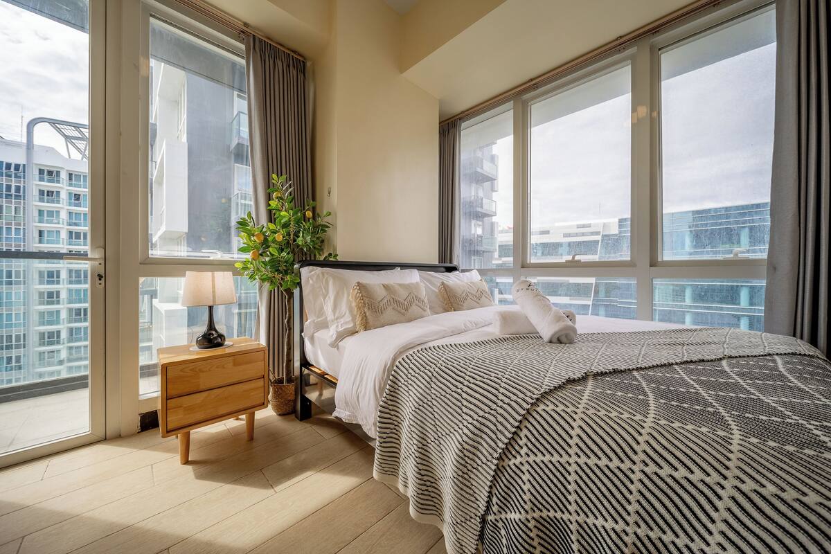 A modern bedroom with a large bed, a nightstand, a lamp, and a potted plant.