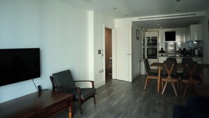 Een moderne woonkamer met een flatscreen televisie, houten meubels en een eethoek met stoelen en een tafel.