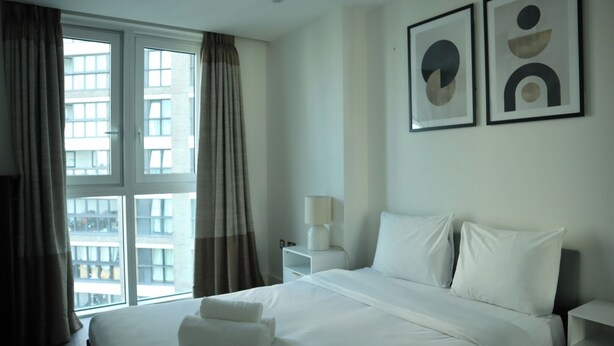 Een hotelkamer met een groot bed, een nachtkastje, een lamp en twee abstracte kunstwerken aan de muur.