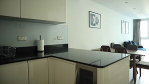 Een moderne keuken met een centraal eiland, een eethoek met tafel en stoelen, en een zithoek met een bank en een raam.
