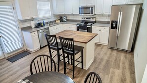 A modern kitchen with white cabinets, stainless steel appliances, a wooden island with chairs, and a checkered table mat.