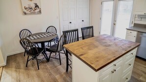 A kitchen with a round table, six chairs, a wooden countertop, and white cabinets.