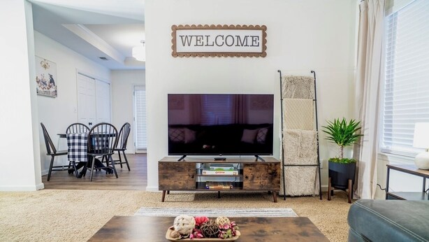 A living room with a TV, a 'WELCOME' sign, a coffee table with decorative items, and a sofa.
