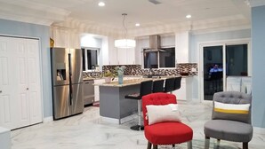 Una cocina moderna con una isla central, electrodomésticos de acero inoxidable y una zona de estar con dos sillas.