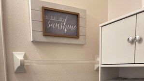Et badeværelse med et håndklædestativ med foldede håndklæder, et inspirerende citat i ramme på væggen og et hvidt skab.