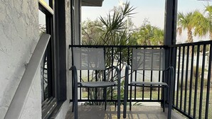 En balkon med bænk, et mønstret tæppe og udsigt til palmer samt en klar himmel.