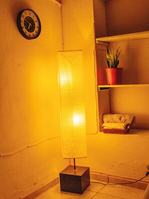 A room with a standing lamp, a clock, a shelf with a potted plant, and a basket with towels.
